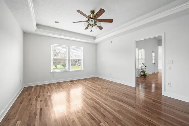 an empty room with wooden floor chandelier fan and windows