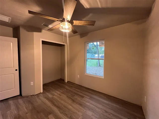 an empty room with wooden floor fan and windows