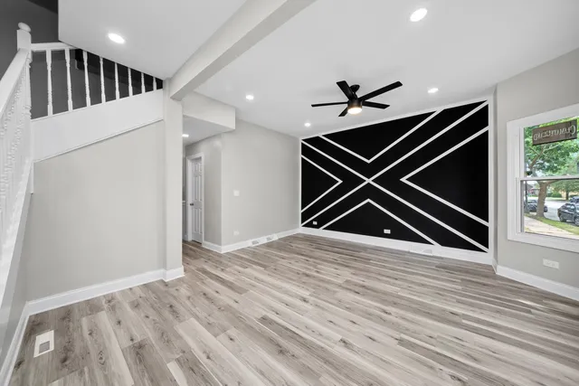 a view of an empty room with wooden floor and ceiling fan
