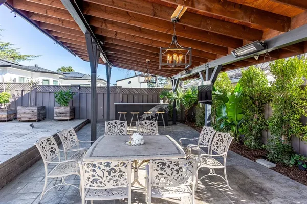 a backyard of a house with table and chairs a barbeque with a bench and trees