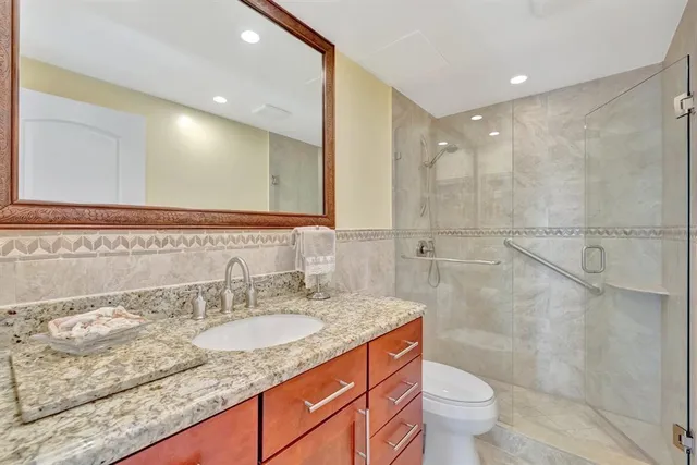 a bathroom with a granite countertop sink a toilet a mirror and shower