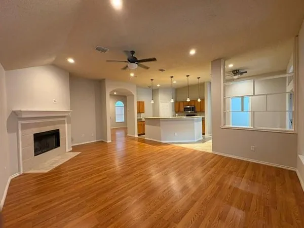 a view of an empty room and kitchen with fireplace wooden floor