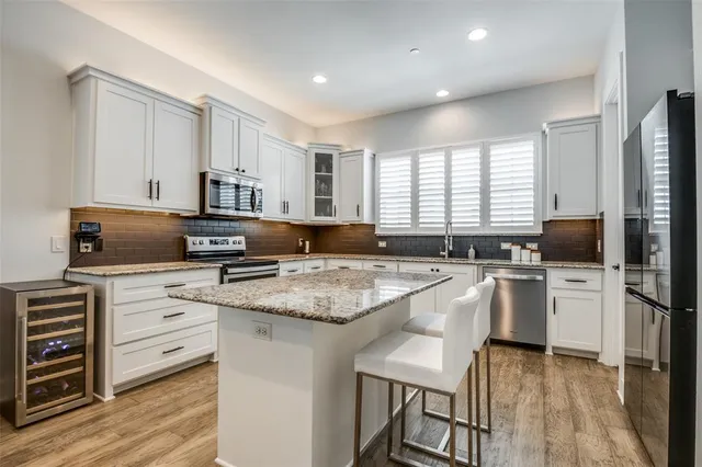 a kitchen with stainless steel appliances granite countertop a stove a sink a microwave a refrigerator a stove and white cabinets with wooden floor