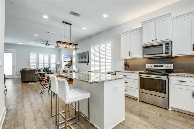 a kitchen with stainless steel appliances granite countertop a stove top oven a sink dishwasher a dining table and chairs with wooden floor