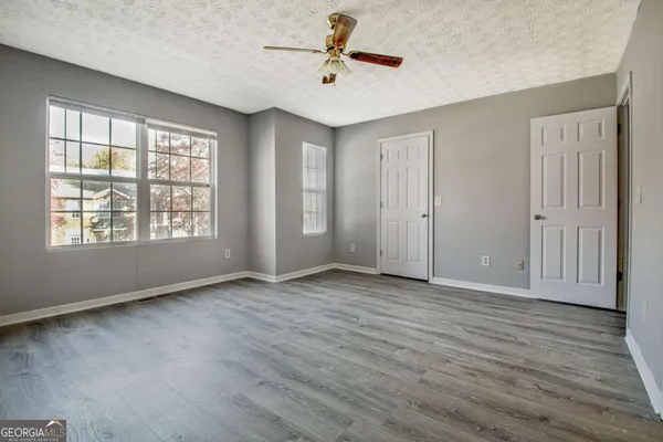 an empty room with wooden floor ceiling fan and windows