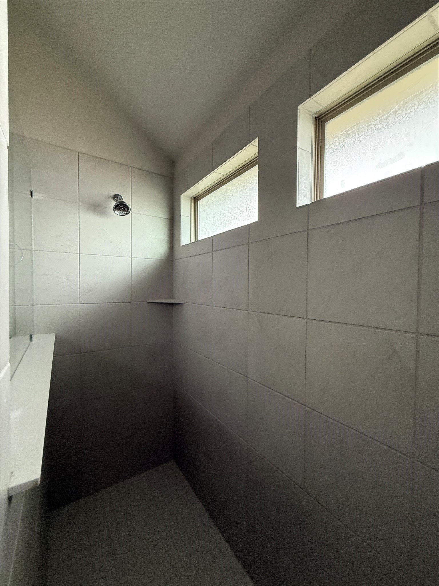 31961 Retama Rnch Drive Spring, TX 77386 - Photo 21 of 25 This photo shows a modern, tiled shower with high ceilings and natural light from two horizontal windows, creating a bright and open feel.