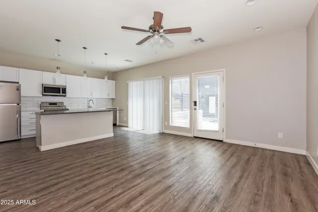 a view of an empty room with kitchen appliances and a ceiling fan
