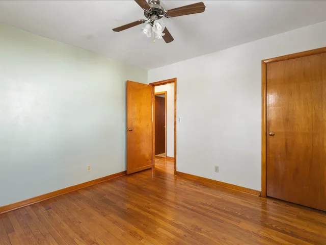 a view of an empty room with wooden floor and a ceiling fan