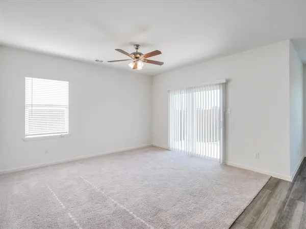 an empty room with chandelier fan and windows