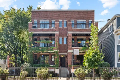 a front view of a building with plants and large trees