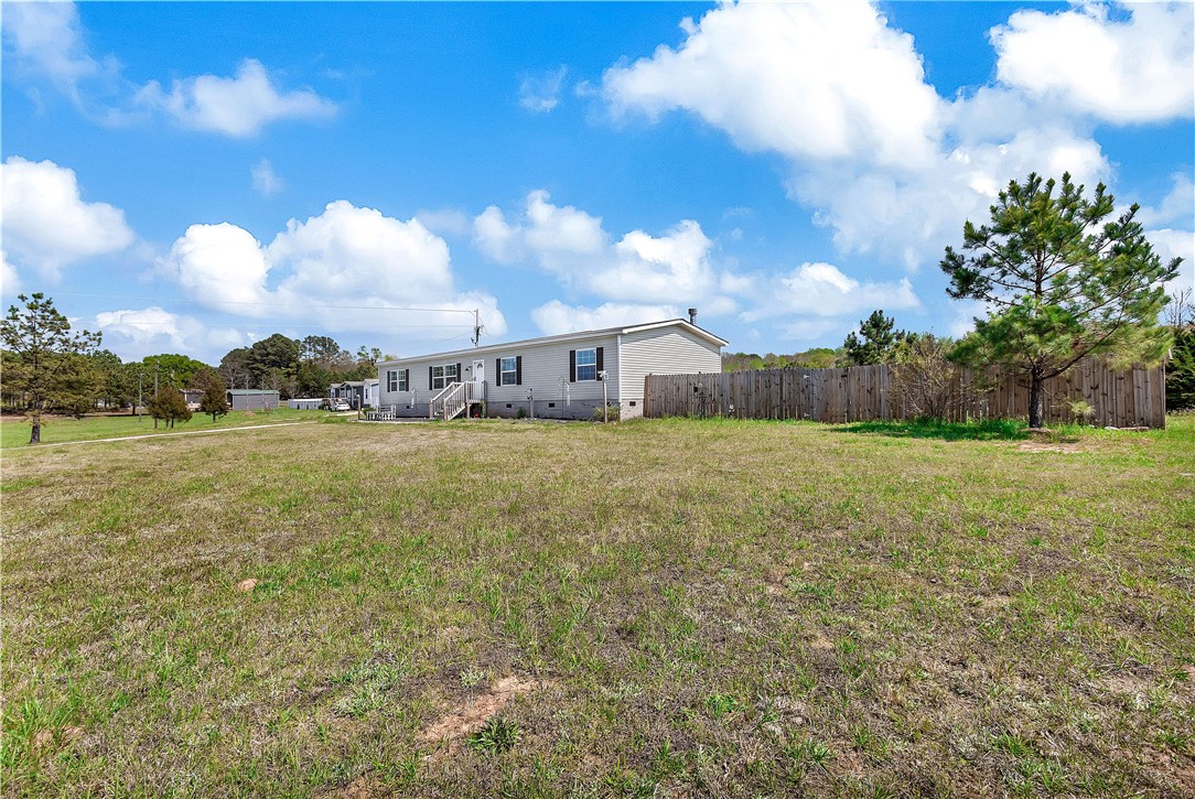 633 Project Road Iva, SC 29655 - Photo 29 of 38 A spacious yard with a charming house and surrounding fence under a bright, cloud-filled sky.