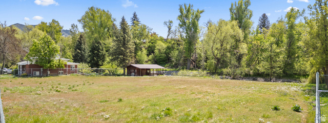 472 East 300 South Logan, UT 84321 - Photo 8 of 9 Expansive open lot featuring a detached outbuilding with covered space, surrounded by mature trees and natural landscaping