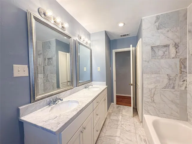 a bathroom with a granite countertop double vanity sink mirror and a bathtub