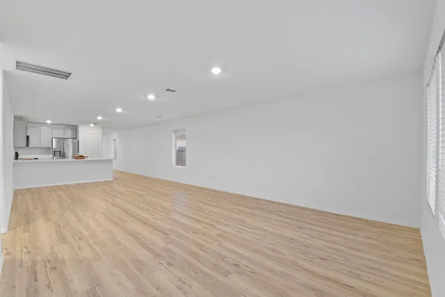 a view of an empty room with wooden floor and a kitchen