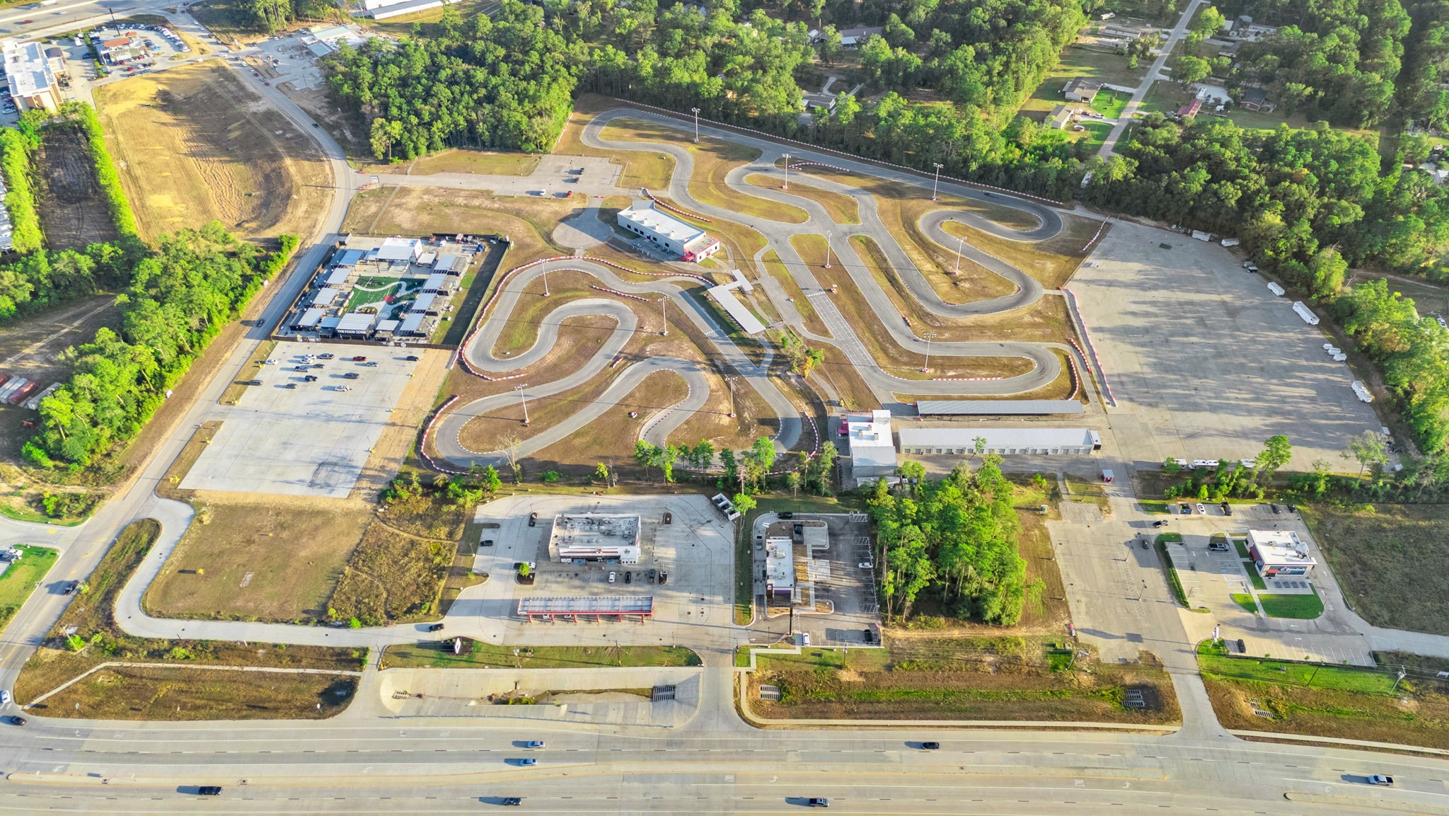22156 Juniper Crossing Drive New Caney, TX 77357 - Photo 46 of 47 This aerial photo showcases a Speedsportz Racing Park, a large go-kart track with winding paths, surrounded by a mix of open spaces and wooded areas. Adjacent to the track is The Food Zone- Grand Texas with a main road providing easy access. The area is a blend of recreational and commercial zones, ideal for motorsport enthusiasts.