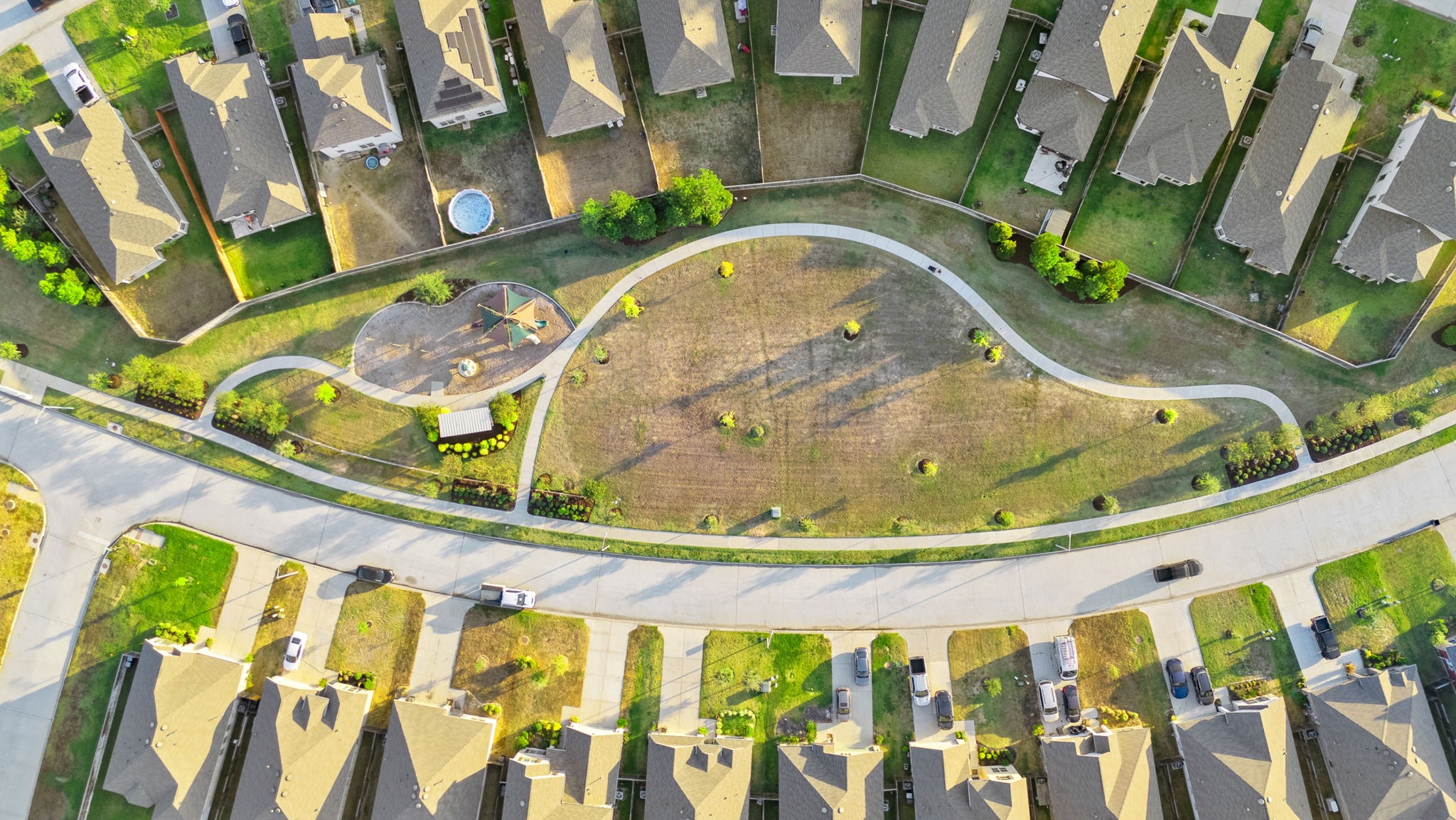 22156 Juniper Crossing Drive New Caney, TX 77357 - Photo 47 of 47 This aerial photo showcases a suburban neighborhood with neatly aligned homes and driveways. A central green space with a playground and walking paths provides a community area, giving the neighborhood a family-friendly appeal.