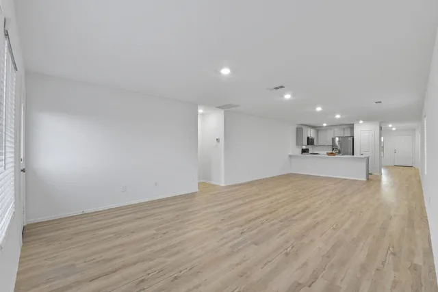 a view of an empty room with wooden floor and a kitchen