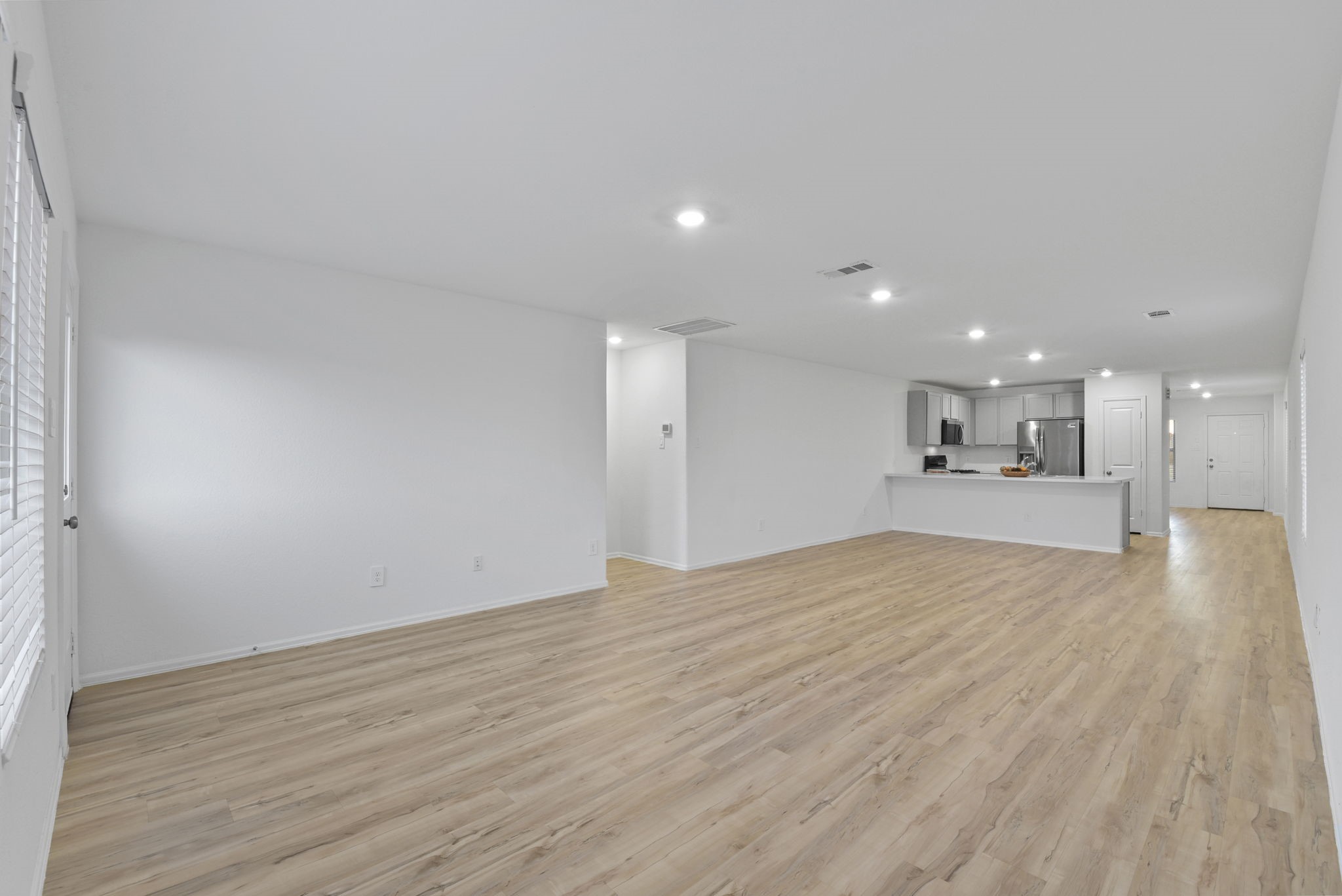 22156 Juniper Crossing Drive New Caney, TX 77357 - Photo 7 of 47 This photo showcases a spacious, open-concept living area with light wood flooring and neutral walls. The layout leads into a modern kitchen with stainless steel appliances and ample counter space. Recessed lighting adds brightness to the room.