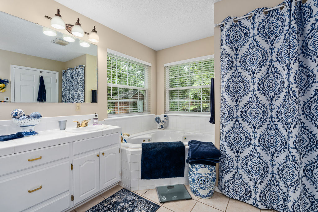 365 Calihan Road Booneville, AR 72927 - Photo 44 of 59 Bathroom featuring a corner jetted tub with tiled surround, a vanity with white cabinetry and gold-tone hardware, a single basin sink, and a large wall-mounted mirror