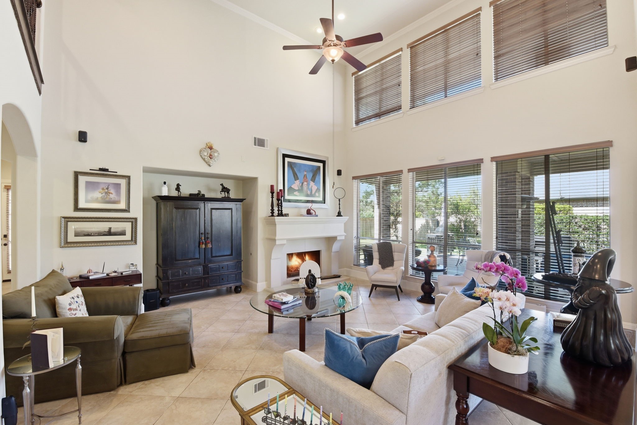 223 South Bauer Point Circle Spring, TX 77389 - Photo 13 of 50 This spacious living room features high ceilings, large windows with ample natural light, and a cozy fireplace. It's elegantly decorated with modern furniture, a ceiling fan, and warm, neutral tones, creating a welcoming atmosphere.