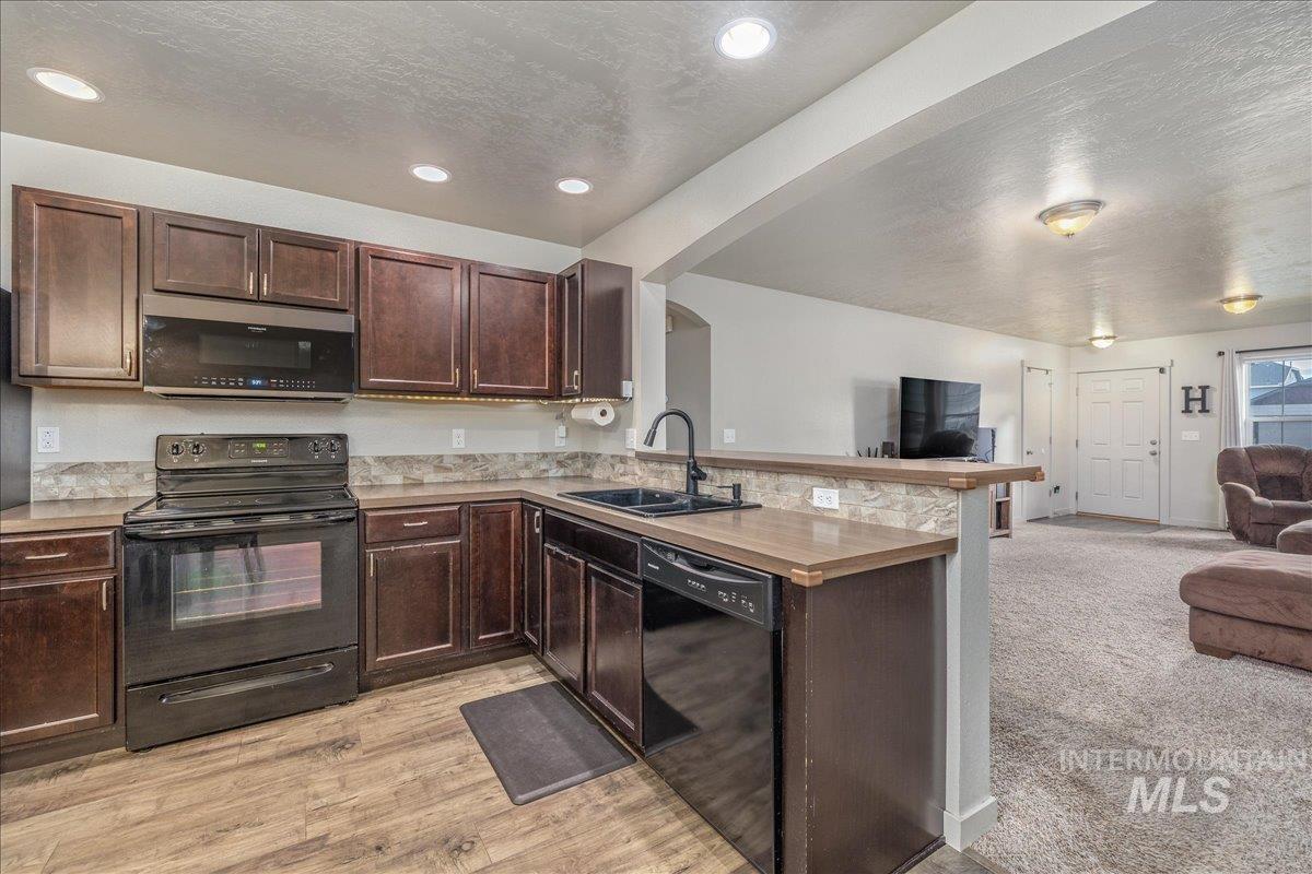 661 North Scotney Avenue Meridian, ID 83642 - Photo 22 of 22 Kitchen featuring black appliances, open floor plan, a textured ceiling, dark brown cabinets, and light countertops