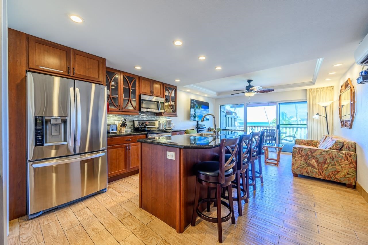 4909 Lower Honoapiilani Road, Unit D6 Lahaina, HI 96761 - Photo 2 of 47 a kitchen with stainless steel appliances kitchen island granite countertop a refrigerator a stove a sink a dining table and chairs with wooden floor