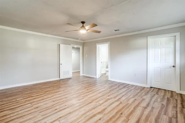 a view of an empty room with wooden floor and a ceiling fan