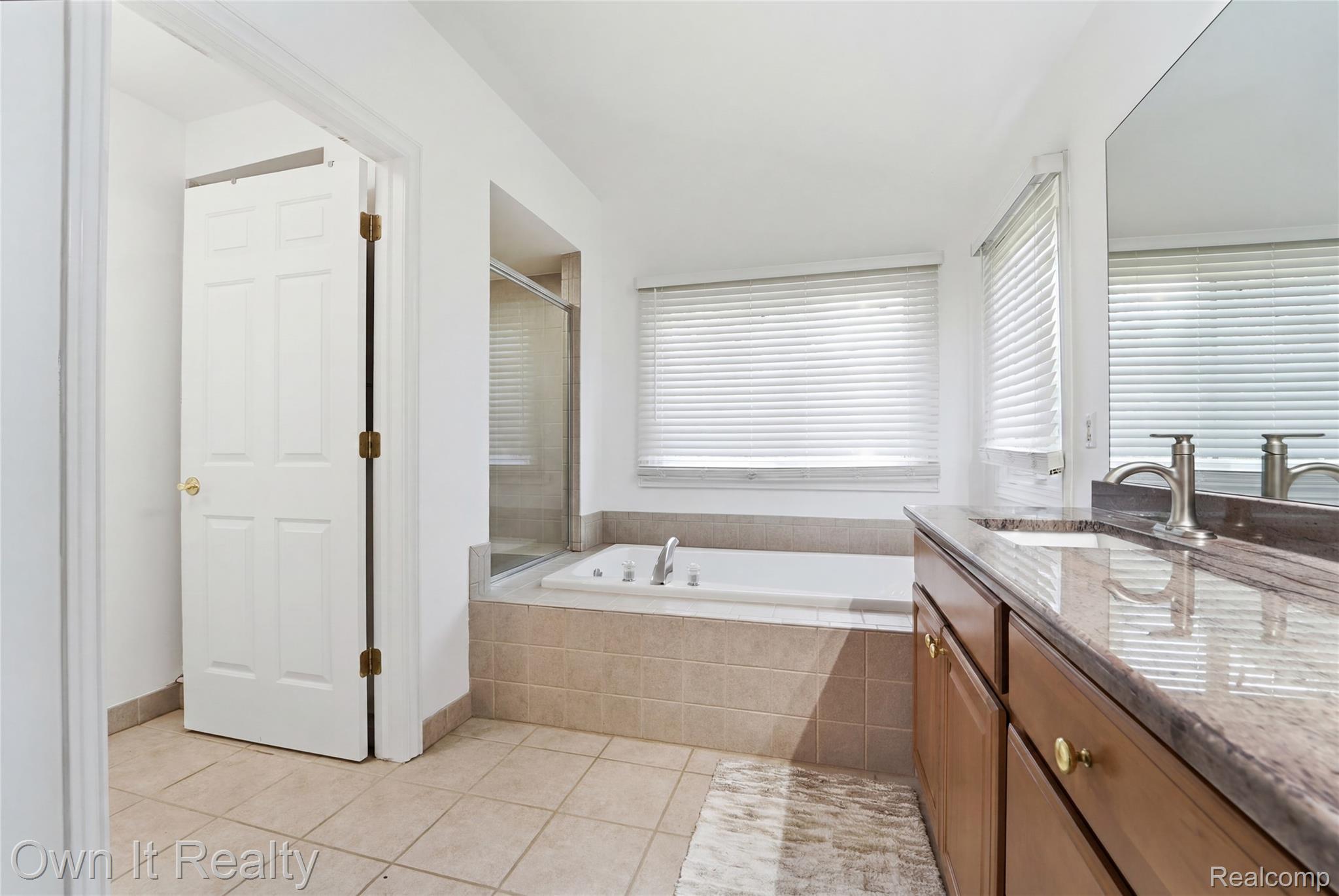 48280 Gladstone Road Canton, MI 48188 - Photo 37 of 59 Bathroom featuring a dual-sink vanity with a stone countertop, a built-in tub with tile surround, a separate glass-enclosed shower, and tiled flooring