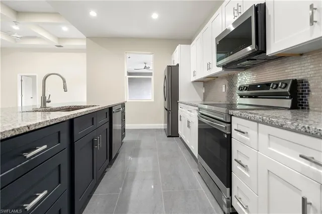 a large kitchen with stainless steel appliances granite countertop a stove a sink dishwasher and a microwave oven with white cabinets