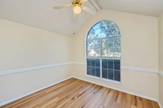 an empty room with wooden floor fan and windows