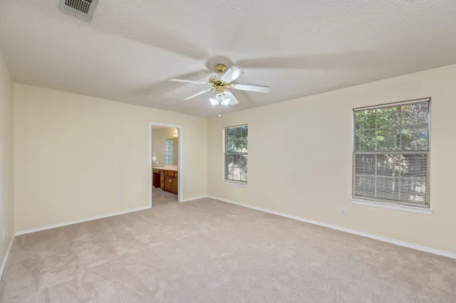 an empty room with chandelier fan and windows