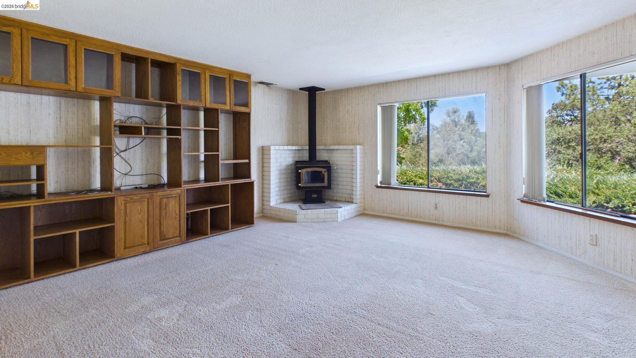23686 Marble Quarry Road, Unit 72 Columbia, CA 95310 - Photo 15 of 35 Built-in shelving and cabinetry with glass-front uppers, corner wood-burning stove with a brick surround, and large windows with integrated blinds