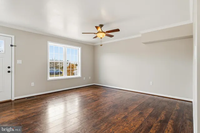 an empty room with wooden floor chandelier fan and windows