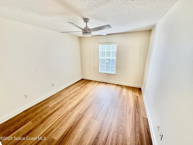 an empty room with wooden floor fan and windows