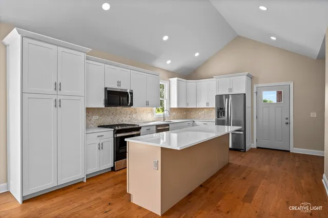 a large kitchen with stainless steel appliances granite countertop a stove top oven a refrigerator a sink and dishwasher with wooden floor