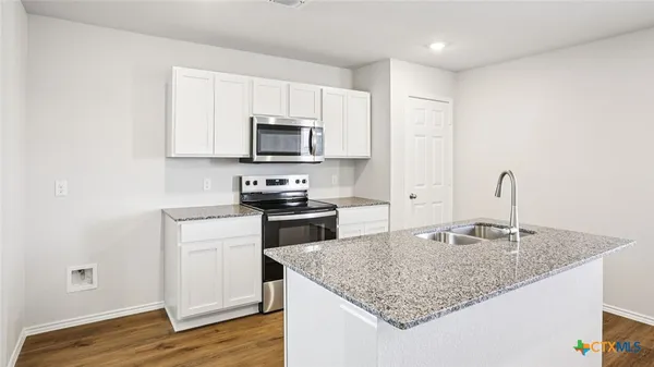 a kitchen with kitchen island granite countertop a sink dishwasher a stove top oven a refrigerator with grey cabinets and wooden floor