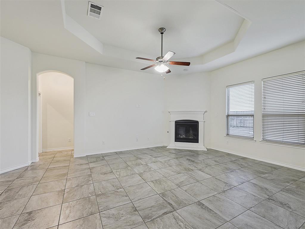 421 Maverick Street Anna, TX 75409 - Photo 11 of 25 Unfurnished living room featuring arched walkways, a ceiling fan, a glass covered fireplace, and a tray ceiling