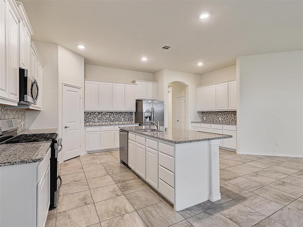 421 Maverick Street Anna, TX 75409 - Photo 6 of 25 Kitchen with decorative backsplash, stainless steel appliances, white cabinetry, arched walkways, and light stone countertops