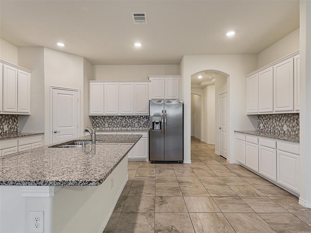 421 Maverick Street Anna, TX 75409 - Photo 7 of 25 Kitchen with arched walkways, decorative backsplash, light stone countertops, stainless steel refrigerator with ice dispenser, and white cabinetry