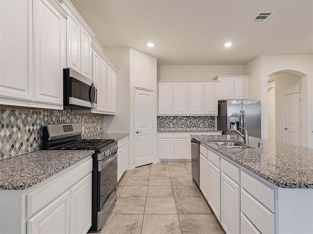 421 Maverick Street Anna, TX 75409 - Photo 8 of 25 Kitchen with stainless steel appliances, white cabinetry, arched walkways, light stone counters, and recessed lighting