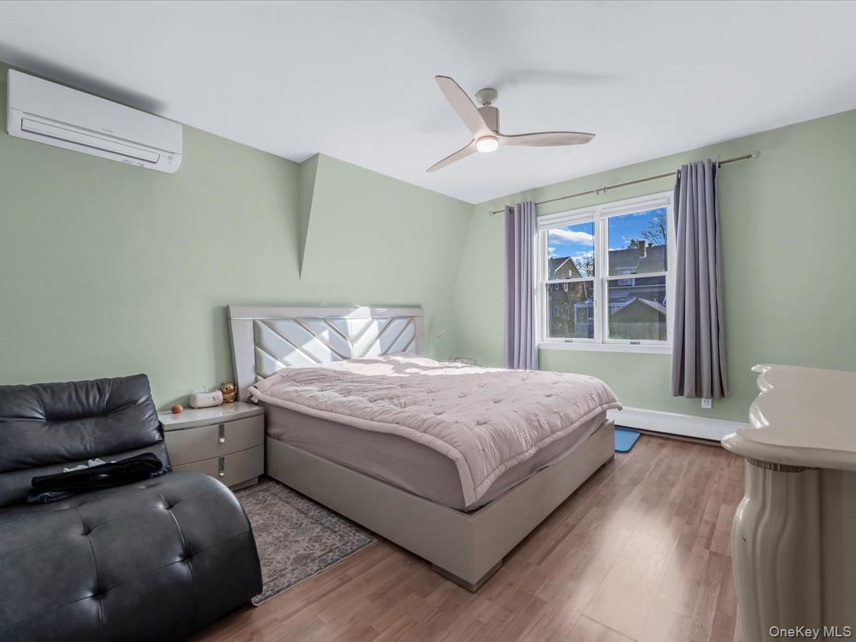 217-32 Corbett Road Queens, NY 11361 - Photo 13 of 25 Bedroom with a wall unit AC, wood finished floors, ceiling fan, and a baseboard heating unit