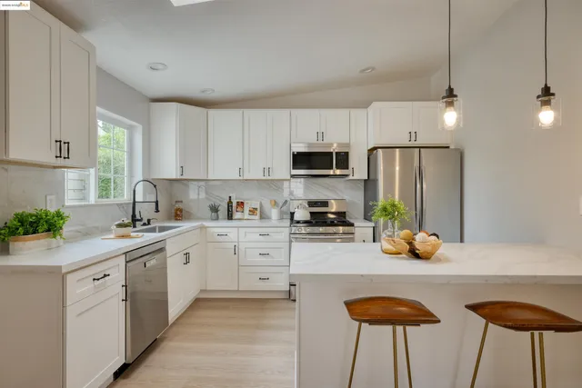 a kitchen with stainless steel appliances a sink a stove a refrigerator cabinets and chairs