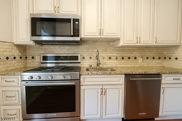 a kitchen with stainless steel appliances granite countertop white cabinets and a stove top oven