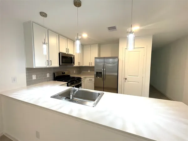 a kitchen with granite countertop a refrigerator a sink a stove a microwave a counter top space and cabinets