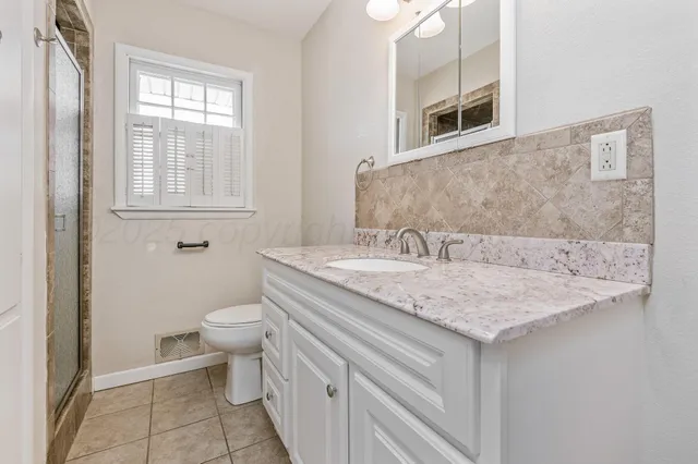 a bathroom with a granite countertop sink a toilet and a window