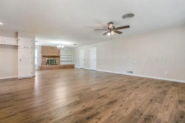 an empty room with wooden floor ceiling fan and kitchen view