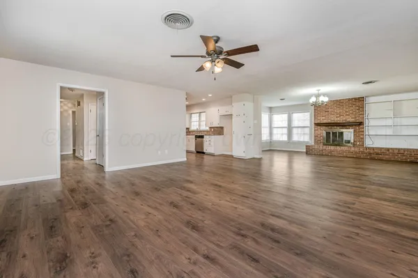 an empty room with wooden floor a ceiling fan and kitchen view