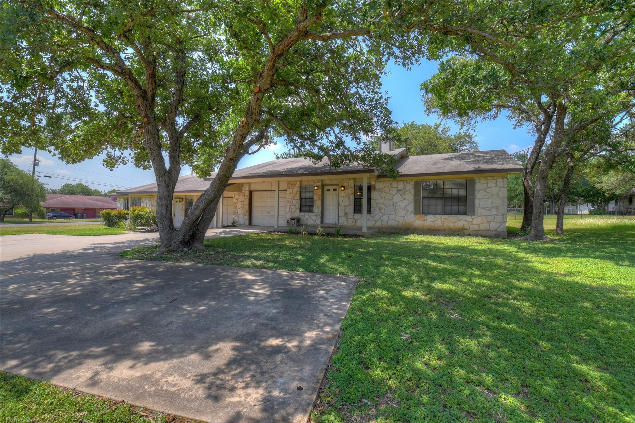 3800 Foust Trail, Unit B Georgetown, TX 78628 - Photo 2 of 16 Mature trees shade this charming stone-clad residence, featuring an attached garage and inviting driveway.
