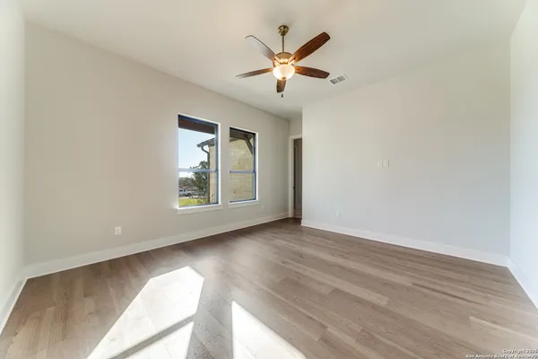 an empty room with wooden floor chandelier fan and windows