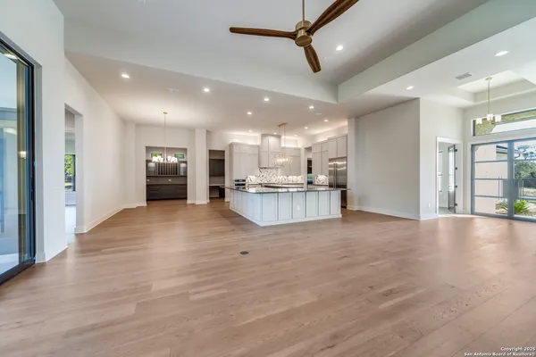 a view of an empty room and kitchen with stainless steel appliances wooden floor